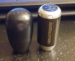 My original vinyl/rubber knob next to the rare Mazdaspeed knob. Not pictured: two wooden Nardi 5-speed knobs